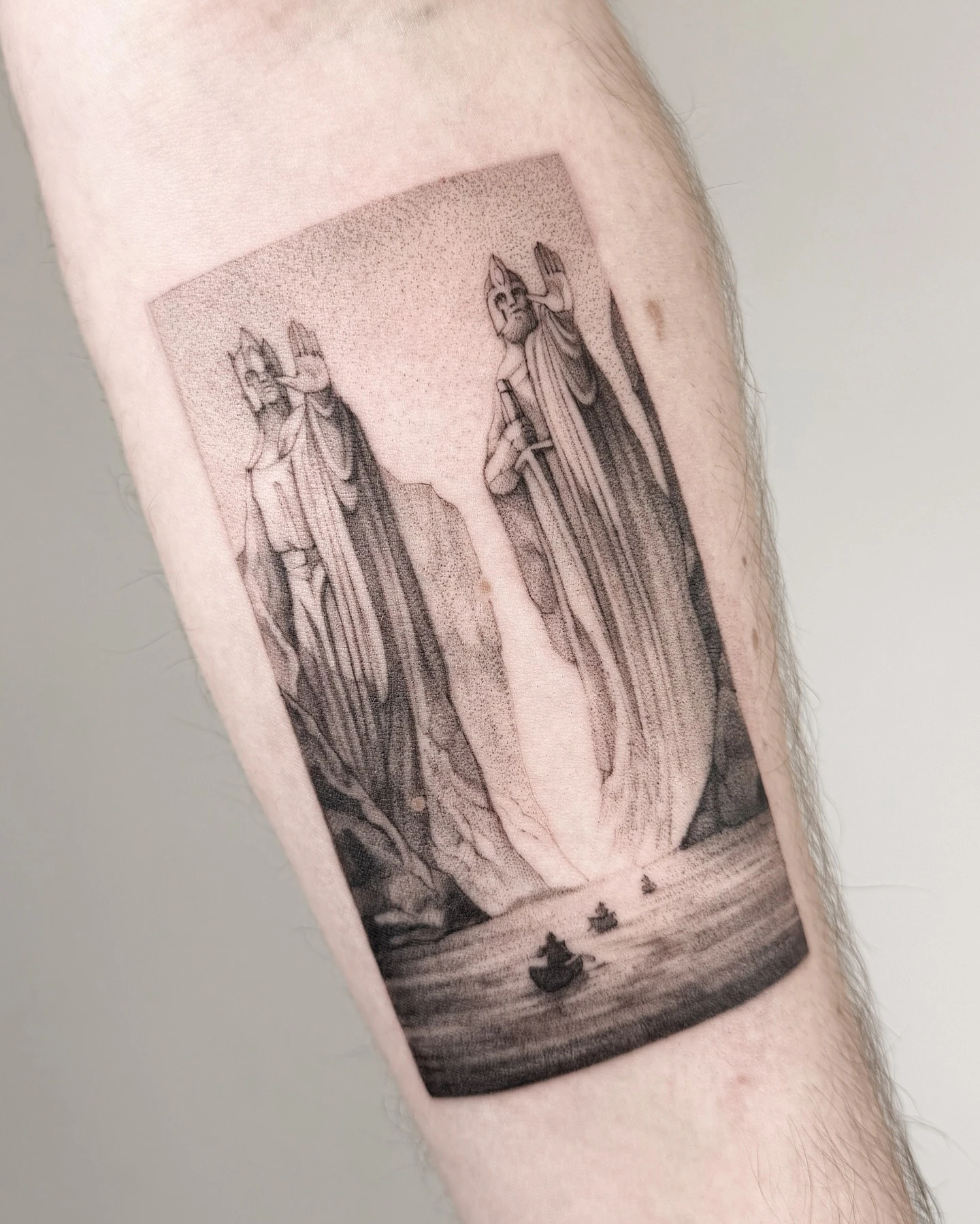Czarno-szary tatuaż przedstawiający Argonath z „Władcy Pierścieni” — dwie monumentalne, odziane w szaty postacie nad wodą i łodziami.