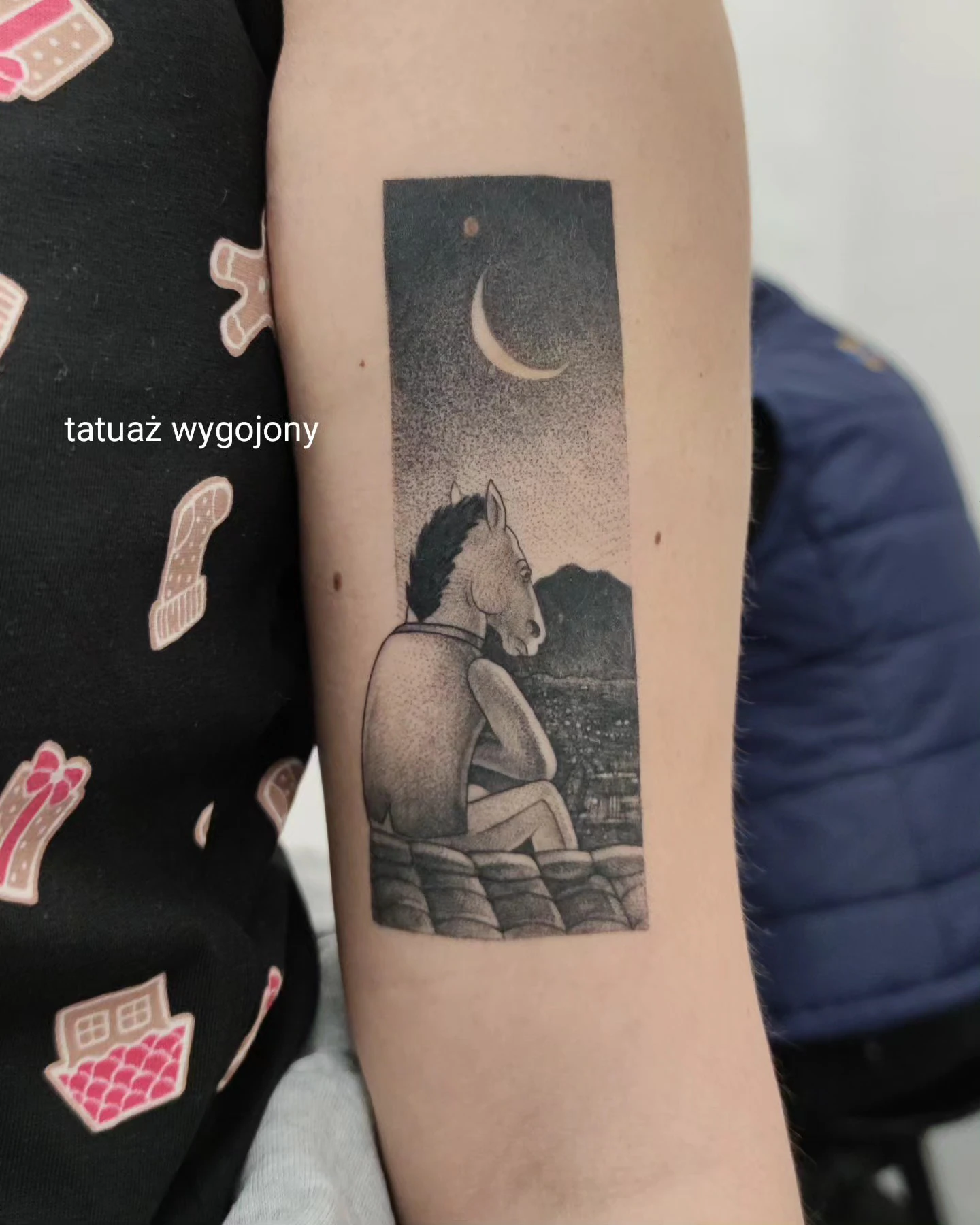 Wygojony tatuaż przedstawiający BoJacka Horsemana siedzącego na tle górskiego krajobrazu, pod sierpem księżyca.
