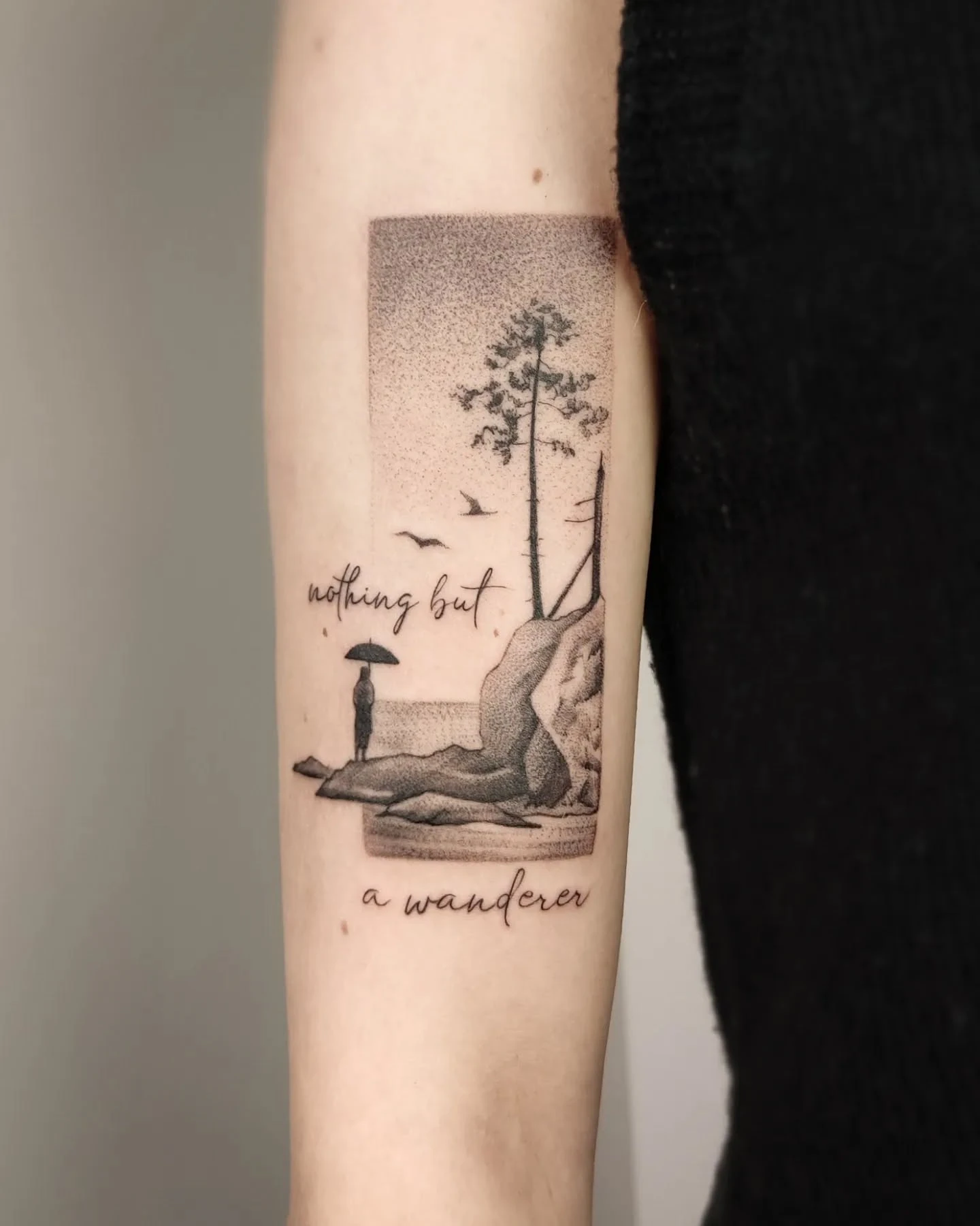 Tatuaż przedstawiający melancholijny pejzaż z drzewem, postacią z parasolem, ptakiem oraz napisem „nothing but a wanderer” na ramieniu.