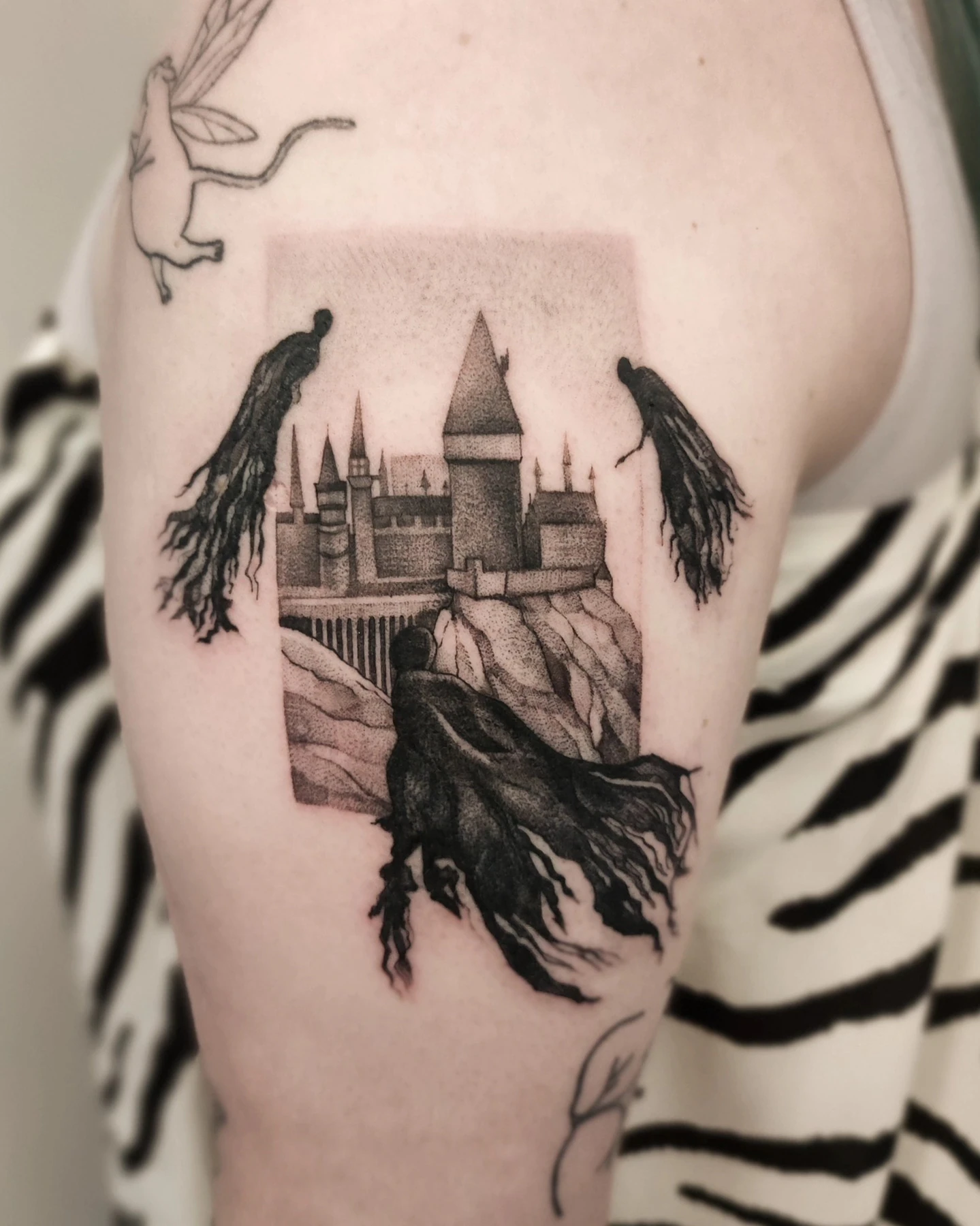 Tatuaż przedstawiający zamek i trzy dementory, inspirowany sceną z Harry’ego Pottera, umieszczony w prostokątnej kompozycji na ramieniu.