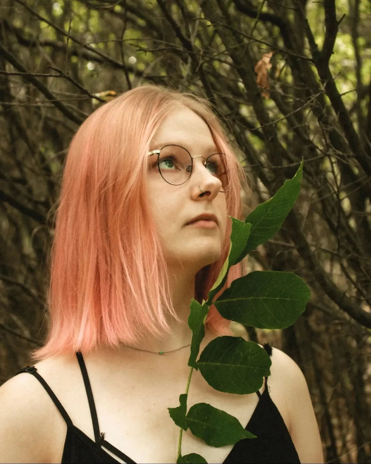 Portret Klary Keczyńskiej w okularach i czarnej sukience, sfotografowanej wśród drzew i wysokich traw; na widocznych ramionach widać tatuaże.