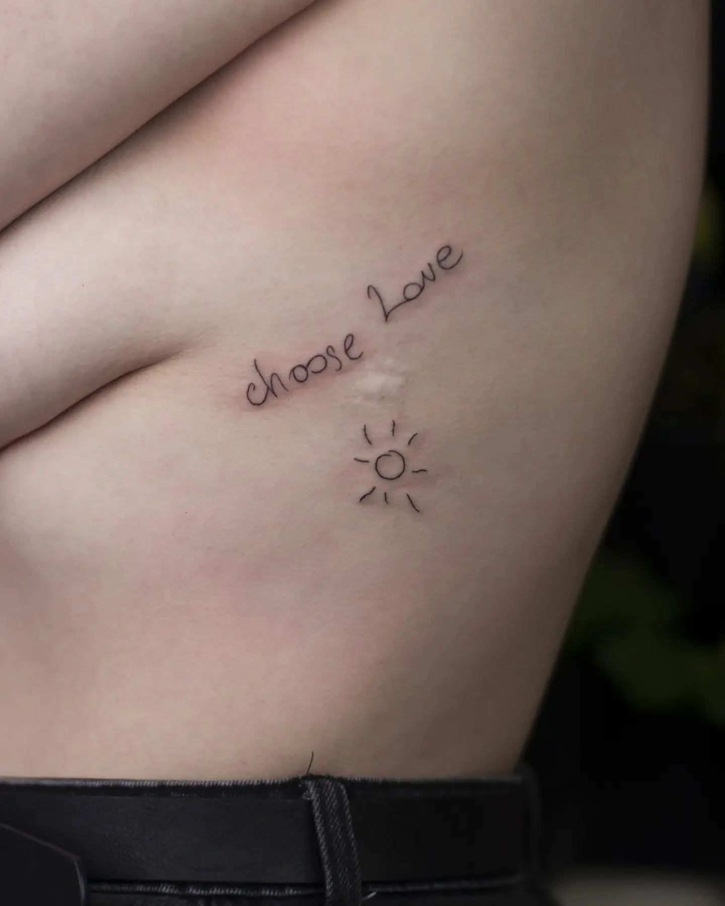Karuzela przedstawia kilka drobnych tatuaży: napis „choose love” z małym symbolem słońca, kwiat na ramieniu oraz niewielki stylizowany motyw zwierzęcy.