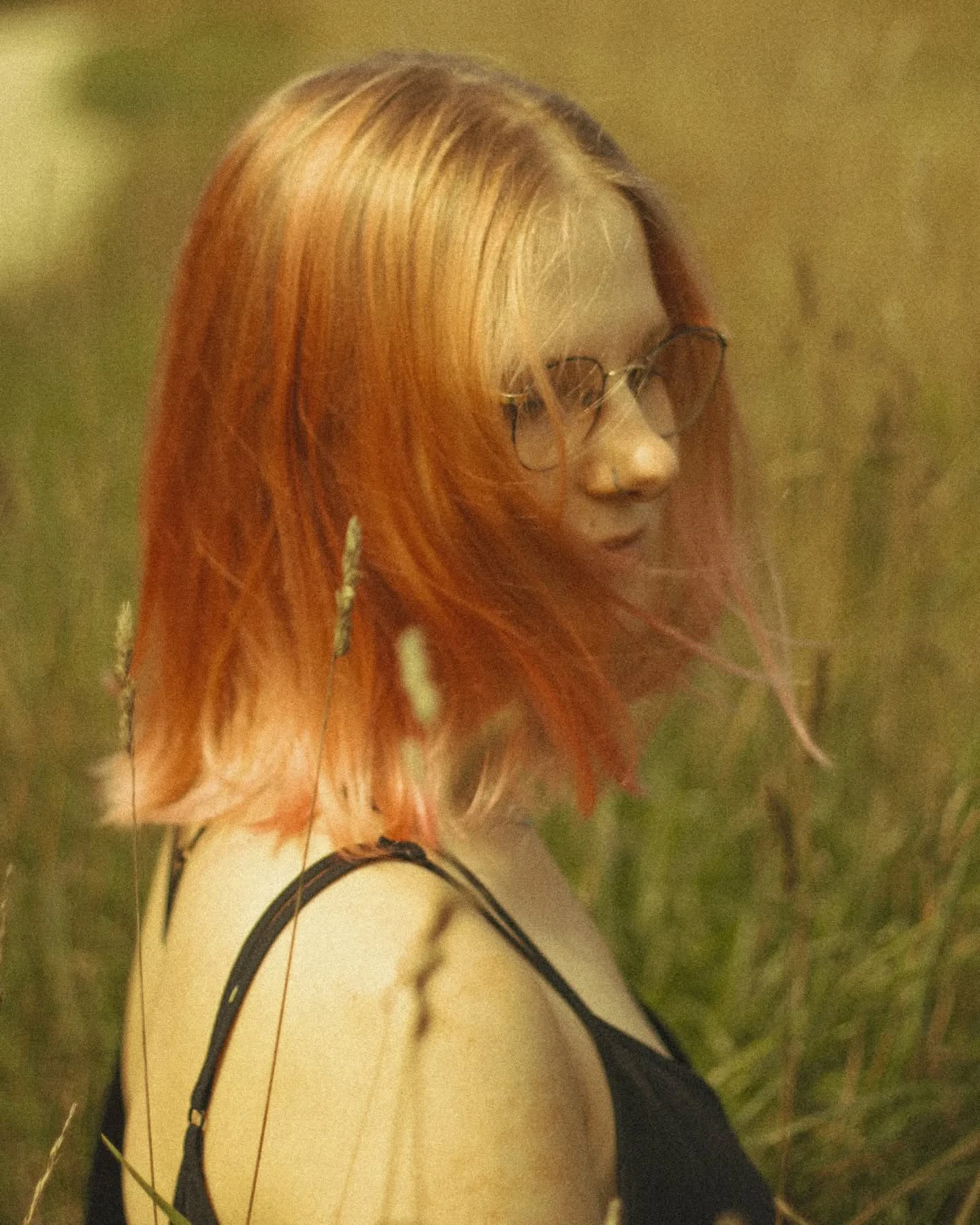 Cztery ujęcia rudowłosej osoby w okularach i czarnym topie, sfotografowanej wśród wysokich traw.