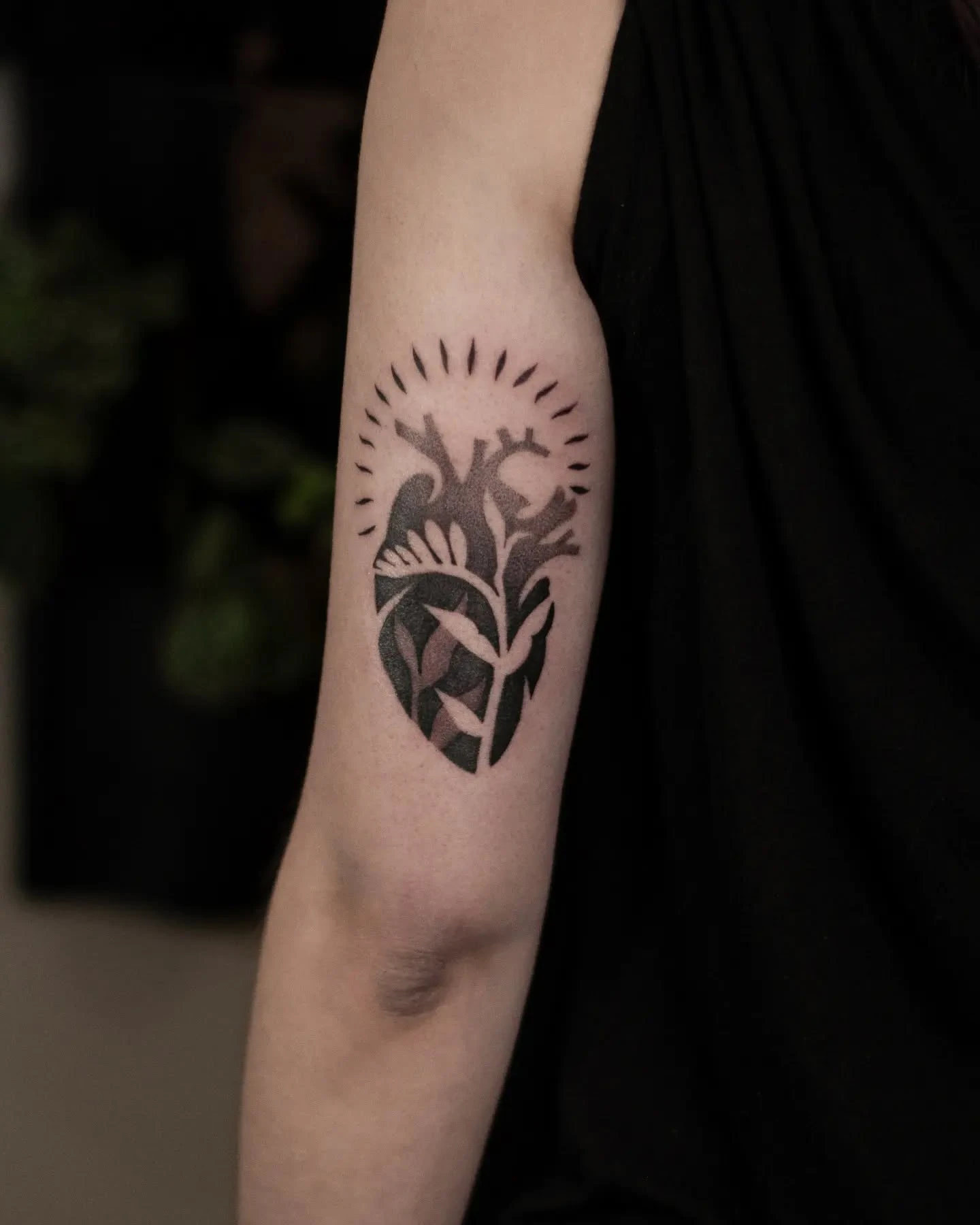 Botaniczne serce wytatuowane na ramieniu, przedstawione na trzech ujęciach, w tym na zbliżeniu.