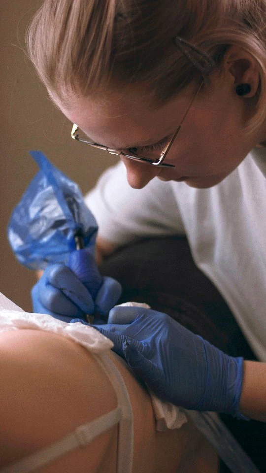 Klatki wideo pokazują pracę tatuatorki nad tatuażem oraz kilka gotowych tatuaży przedstawiających botaniczne motywy, ptaki i inne ilustracyjne elementy.