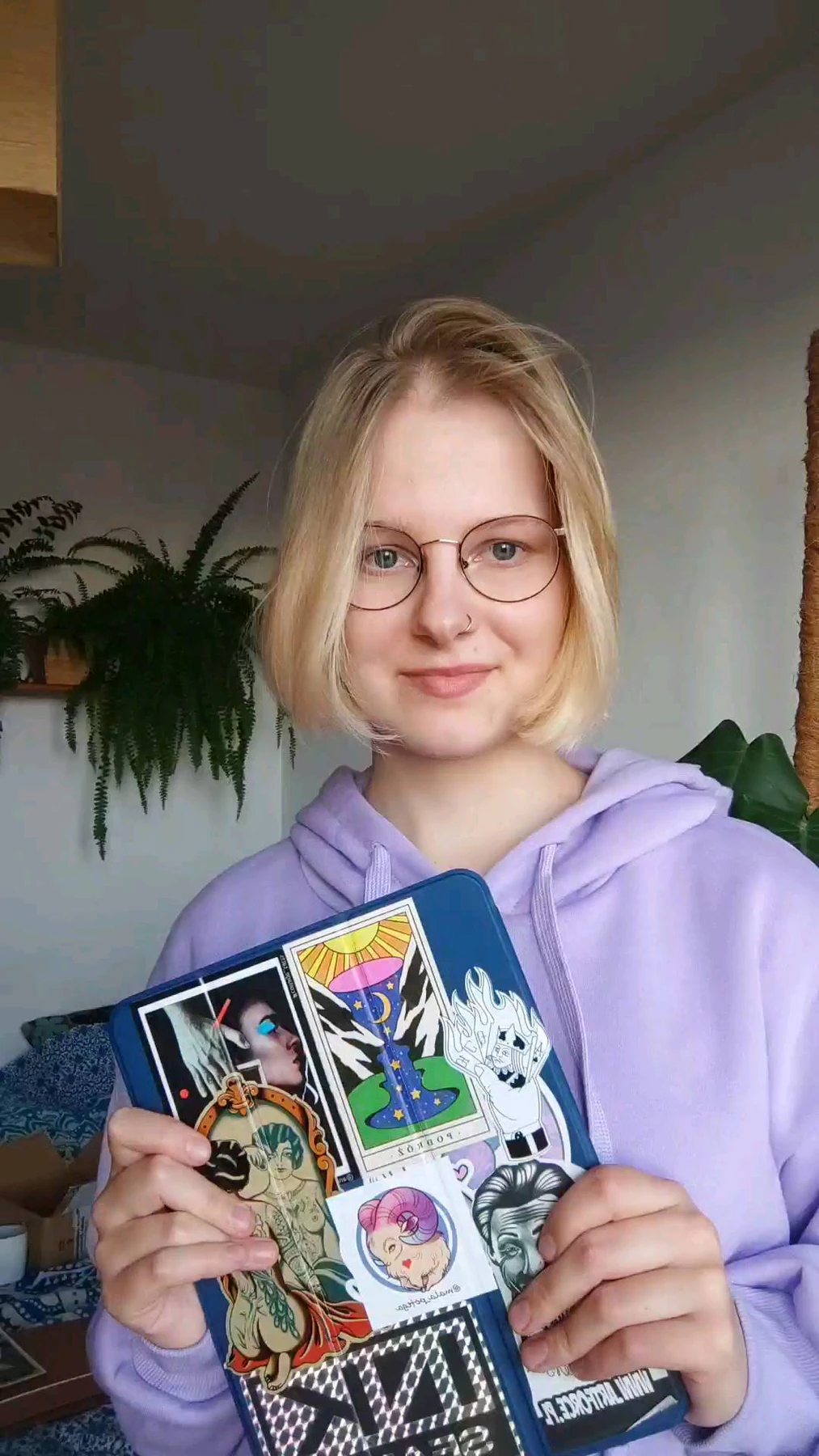 Artystka w okularach pokazuje ozdobiony naklejkami szkicownik, a kolejne kadry prezentują projekty tatuaży z motywami zwierząt oraz kwiatów wyświetlane na tablecie.