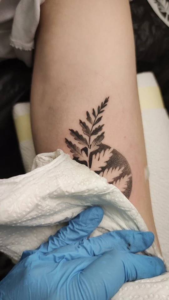 Klatki wideo pokazują kilka tatuaży na nogach i rękach: między innymi botaniczny motyw, owada z ornamentami roślinnymi, abstrakcyjny kształt oraz ciemny fragment innego wzoru; podczas pracy widoczne są rękawiczki tatuatorki.
