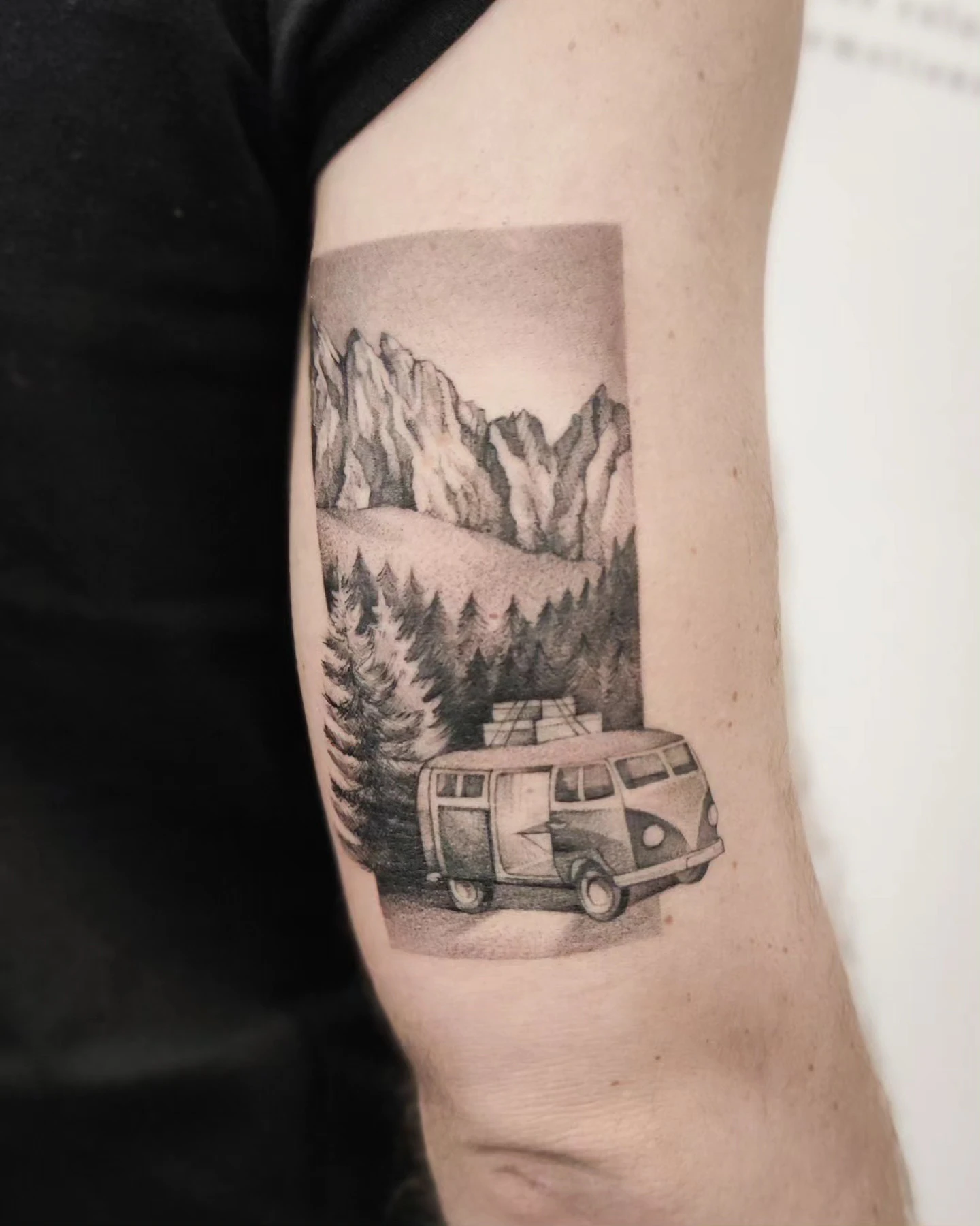 Tatuaż przedstawiający klasycznego Volkswagena T1 na tle gór Dolomitów i leśnego krajobrazu.